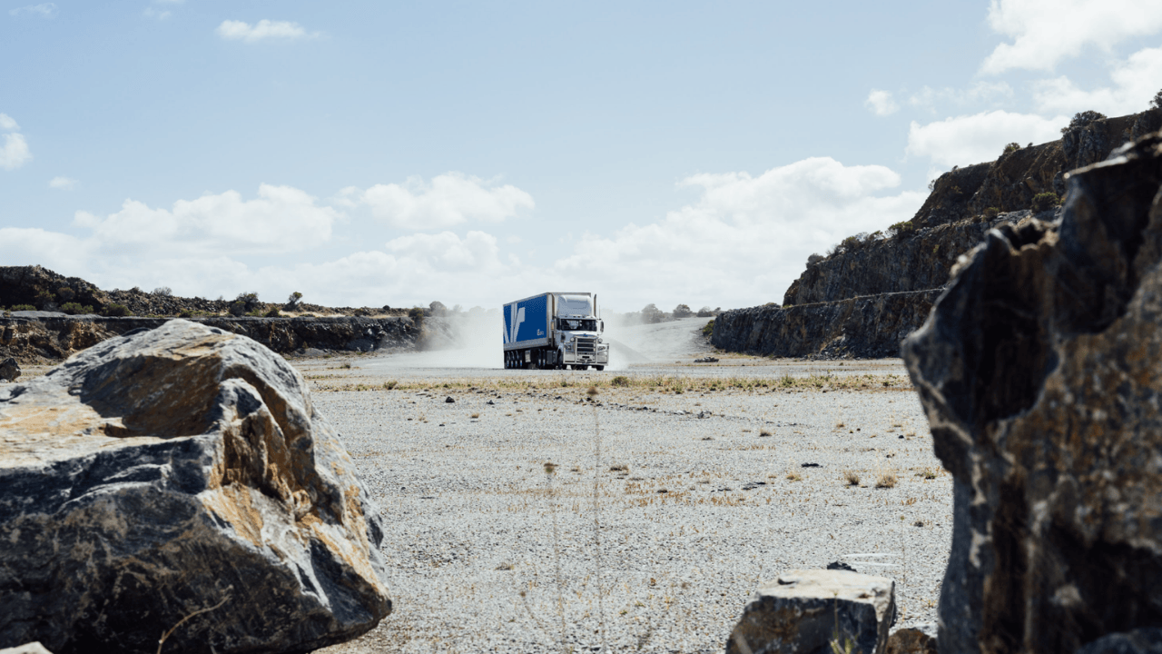 Blue VE Motion truck and trailer driving through a quarry at Rapid Bay, kicking up a cloud of dust.